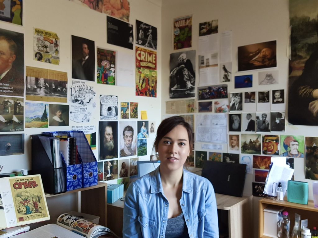 A person sitting in a room with walls covered in various posters and images.